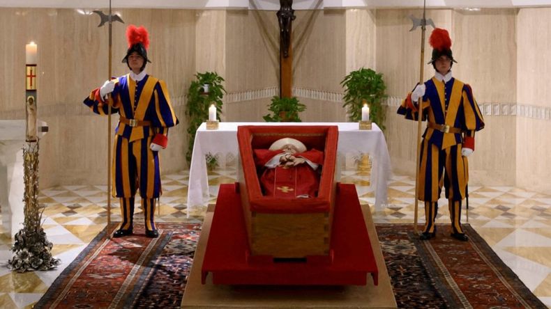Está expuesto en un simple ataúd de madera abierta y en sus manos lleva el rosario. Está expuesto en un simple ataúd de madera abierta y en sus manos lleva el rosario.